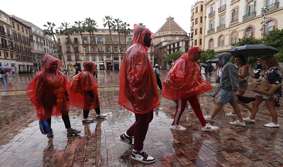 Un grupo de personas se tapan de la lluvia con chubasqueros y paraguas mientras caminan por una calle de Málaga este jueves. EFE.